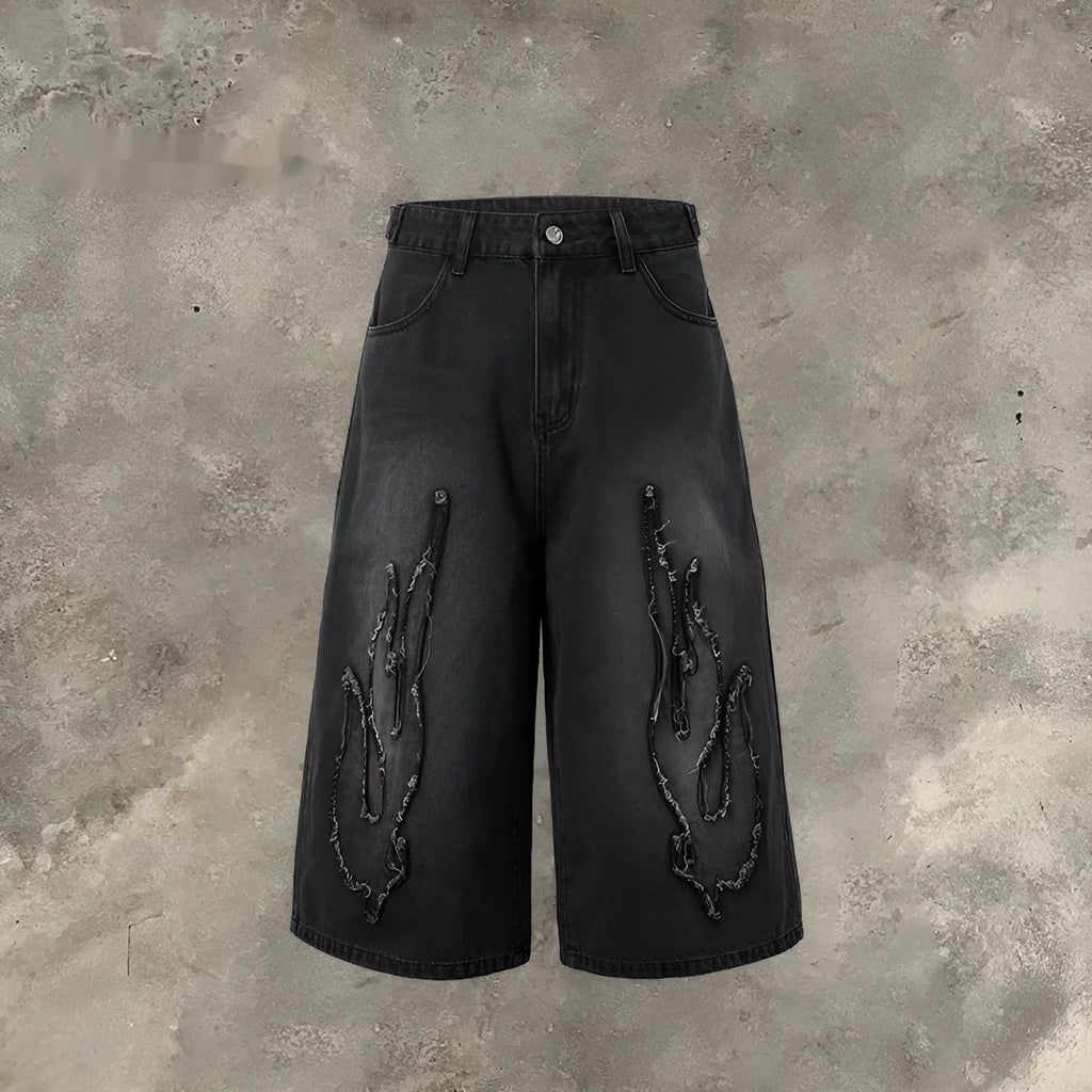 Man wearing black cropped denim shorts with a flame embroidery patch on the leg, street style.