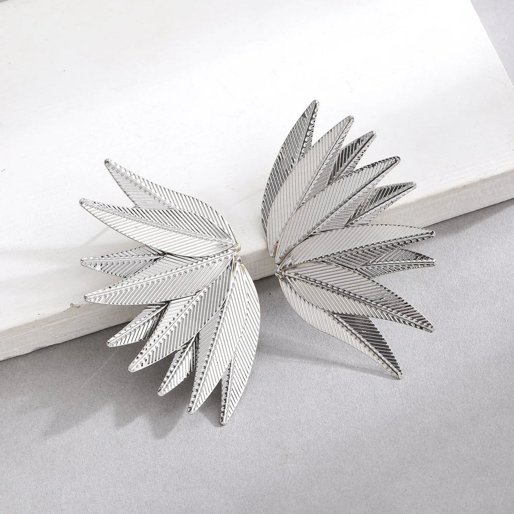 A pair of gold alloy drop earrings shaped like leaves, lying on a surface.