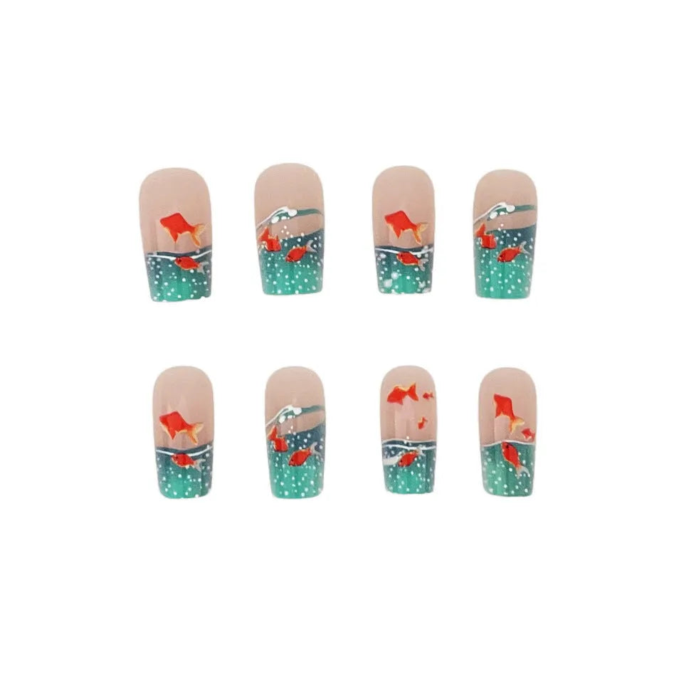 Mid-square blue glaze goldfish nail art pieces with armour design and jelly glue finish on a table