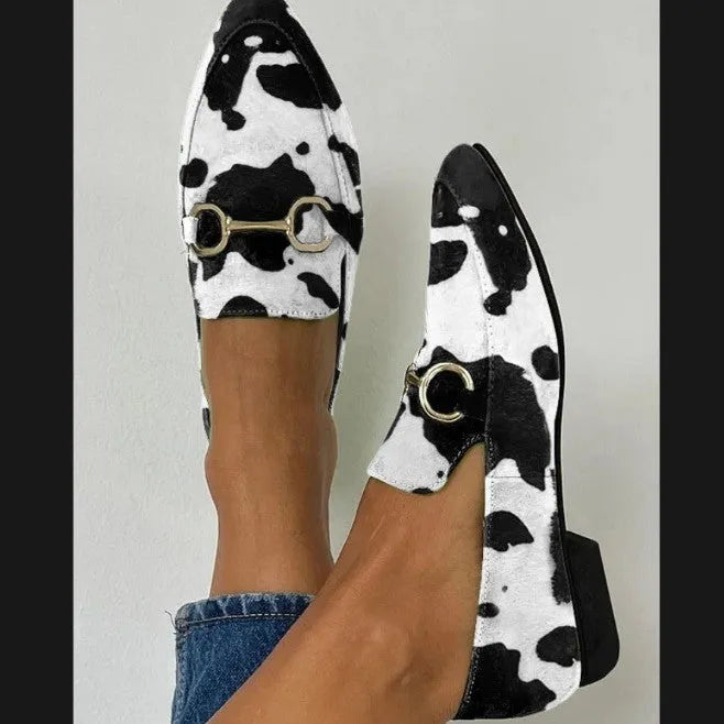 Women's black and white cow pattern pointed-toe mules with flat square heel on a neutral background