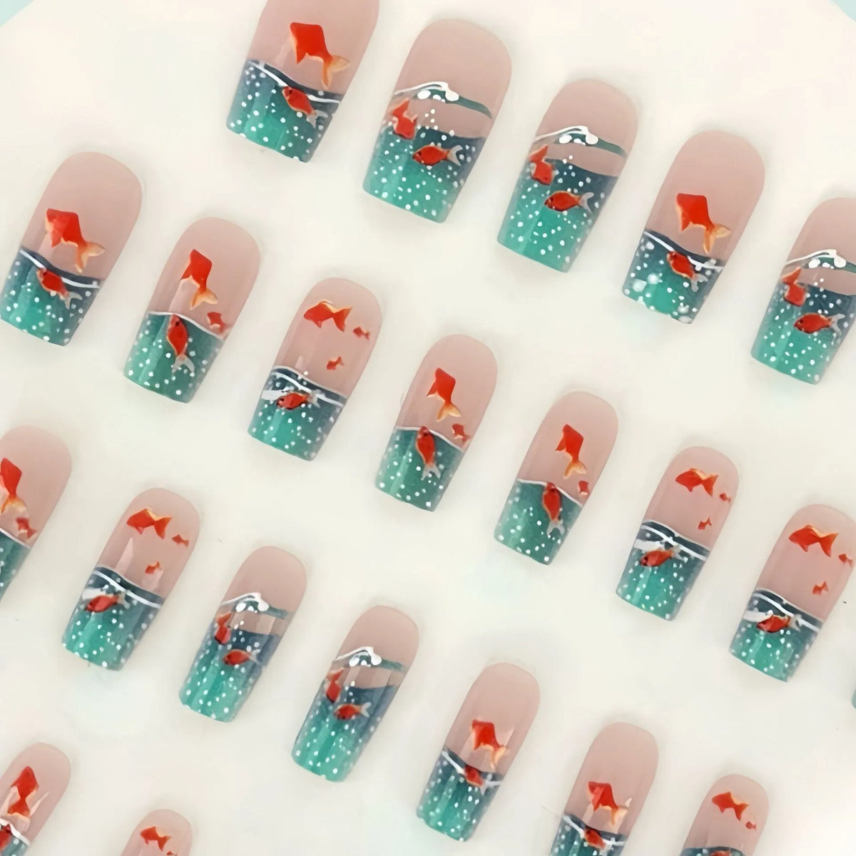 Mid-square blue glaze goldfish nail art pieces with armour design and jelly glue finish on a table