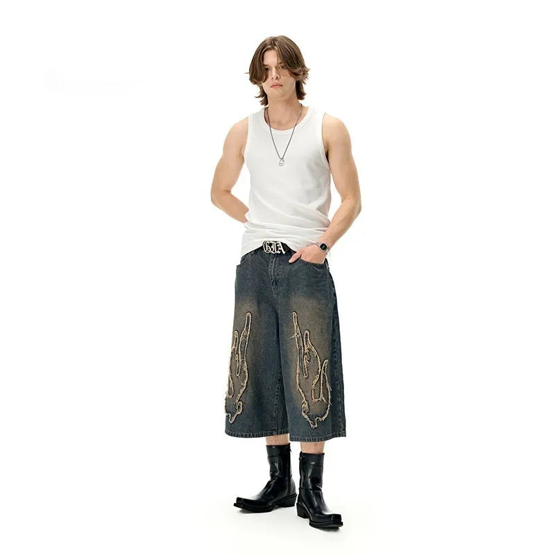 Man wearing black cropped denim shorts with a flame embroidery patch on the leg, street style.