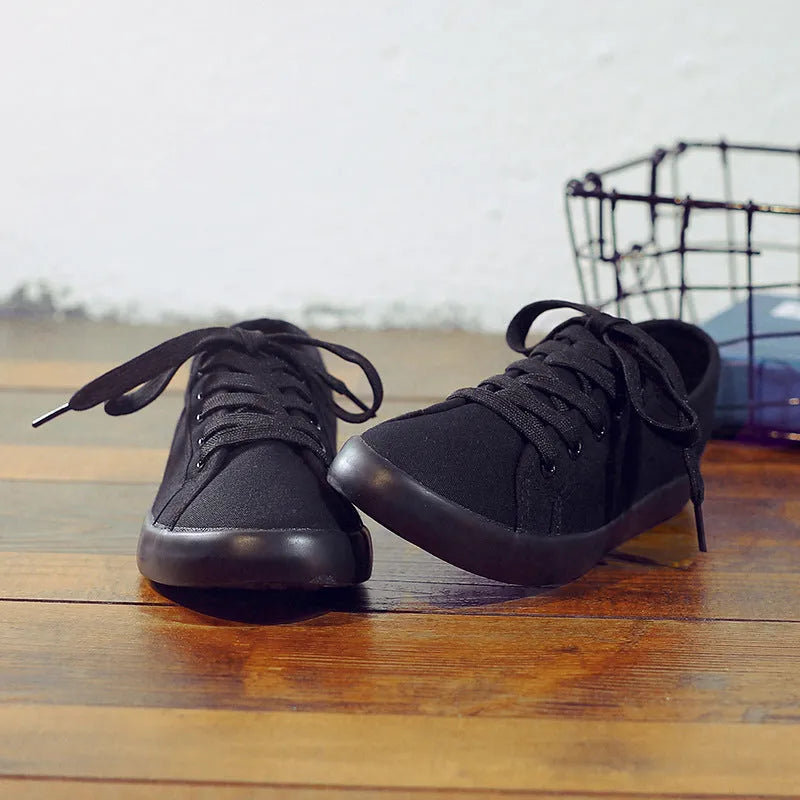 All-black women's low-top canvas shoes with lace-up front and flat rubber sole.