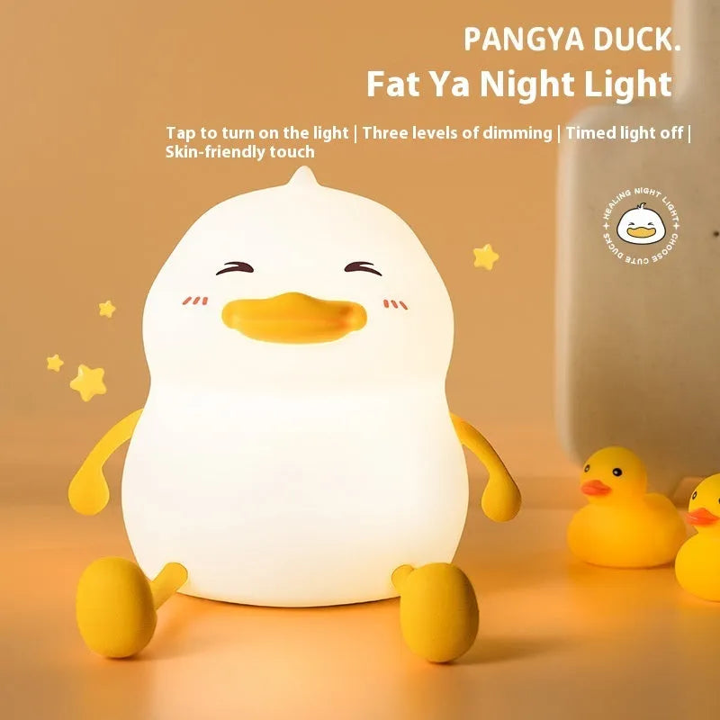Chubby silicone pat night light on desk holding a mobile phone, showing soft glow.