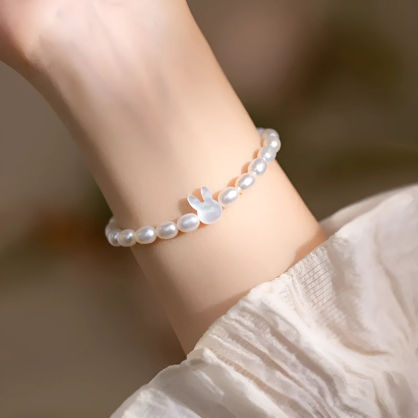 White pearl and silver rabbit charm bracelet on a stretched elastic string showing its adjustable fit.
