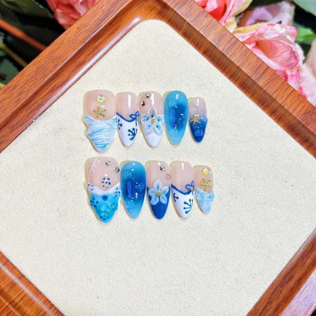 Set of blue false nails with hand-painted colour and carved summer ice design, laid out on a surface.