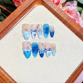Set of blue false nails with hand-painted colour and carved summer ice design, laid out on a surface.