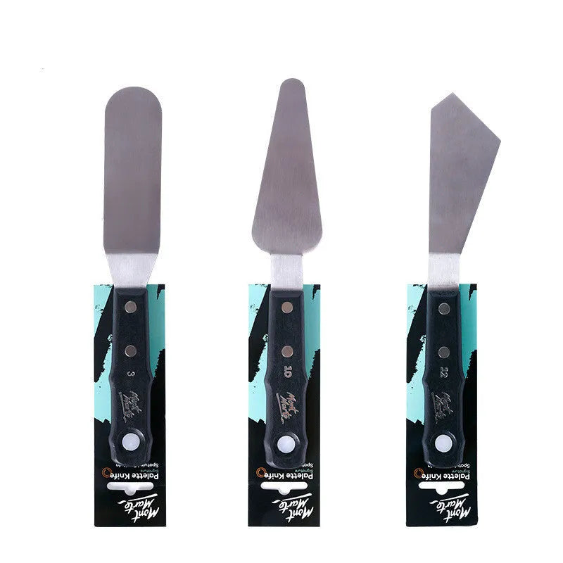 Three stainless steel artist palette knives with different blade sizes on a wooden table.
