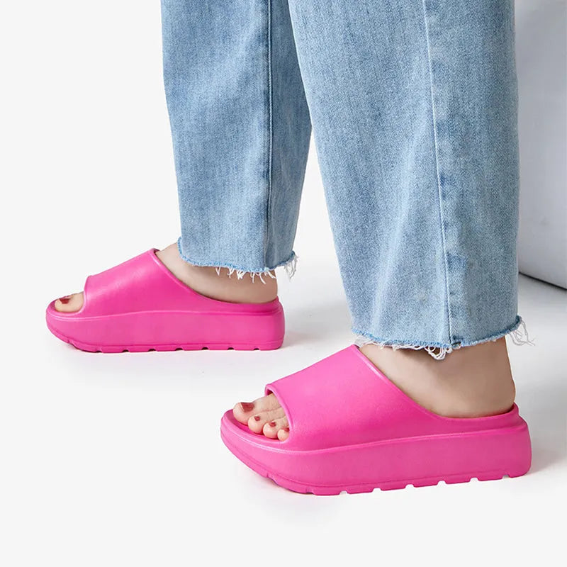 Women's beige open-toe beach slippers with a thick light-coloured sole on a wooden deck.