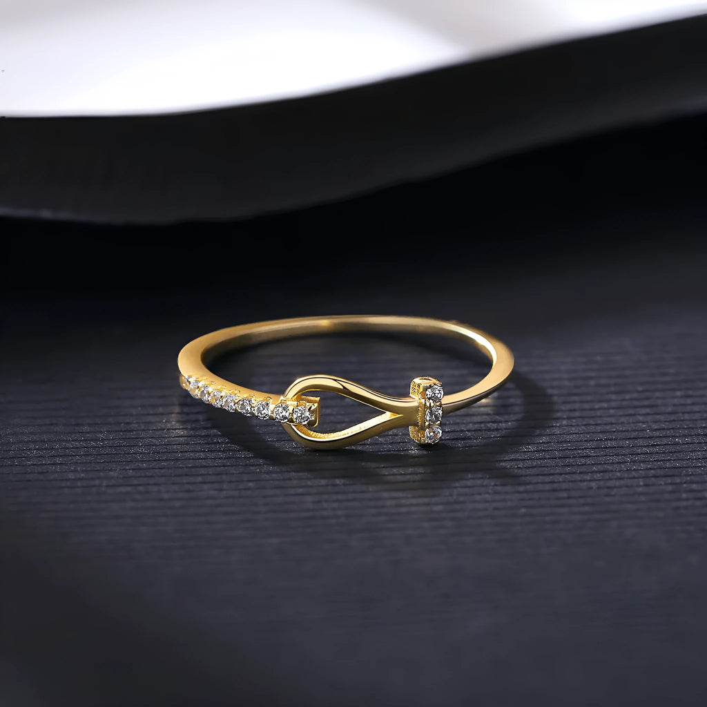Gold electroplated silver bow ring with inlaid zirconium on pink background, front view
