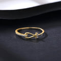 Gold electroplated silver bow ring with inlaid zirconium on pink background, front view