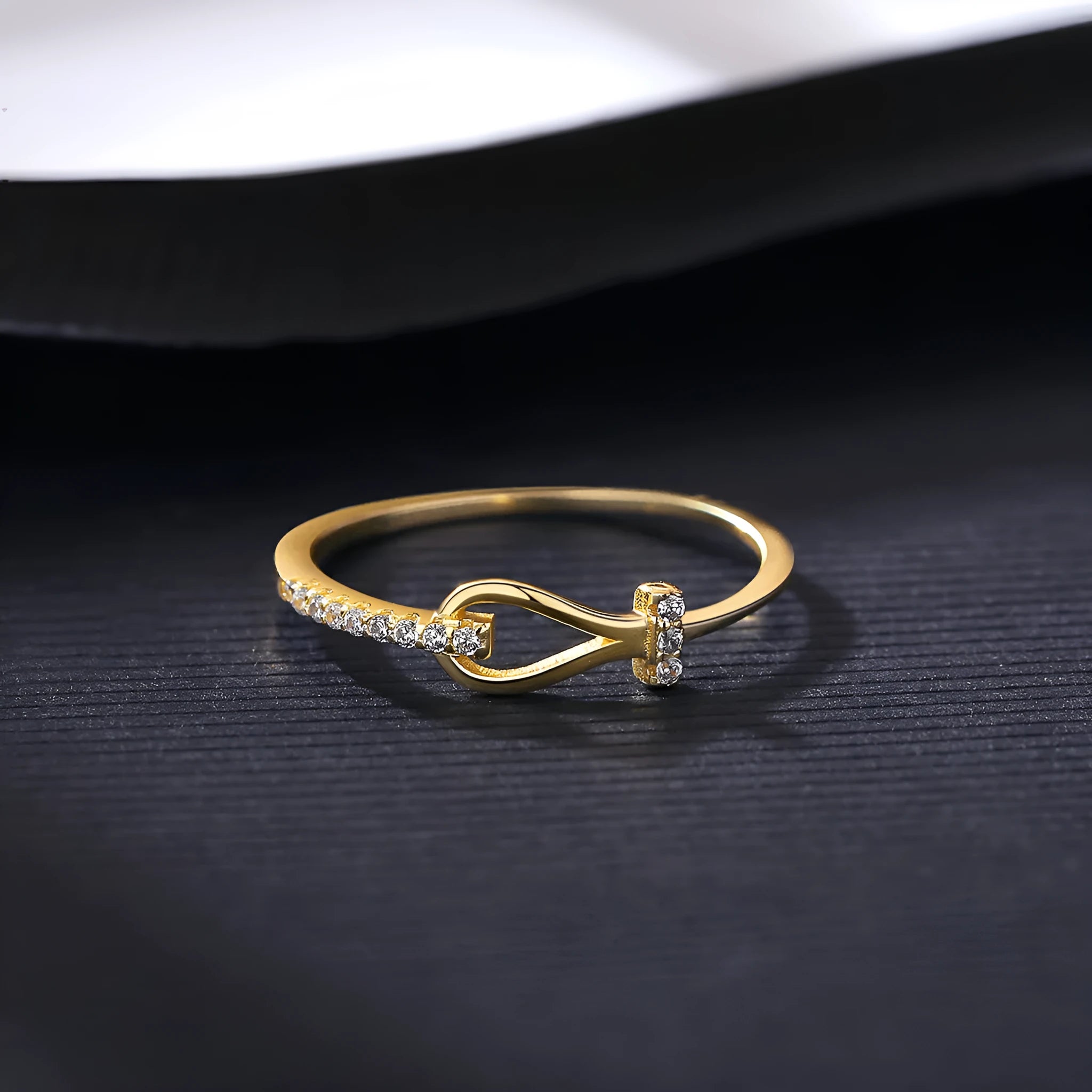 Gold electroplated silver bow ring with inlaid zirconium on pink background, front view
