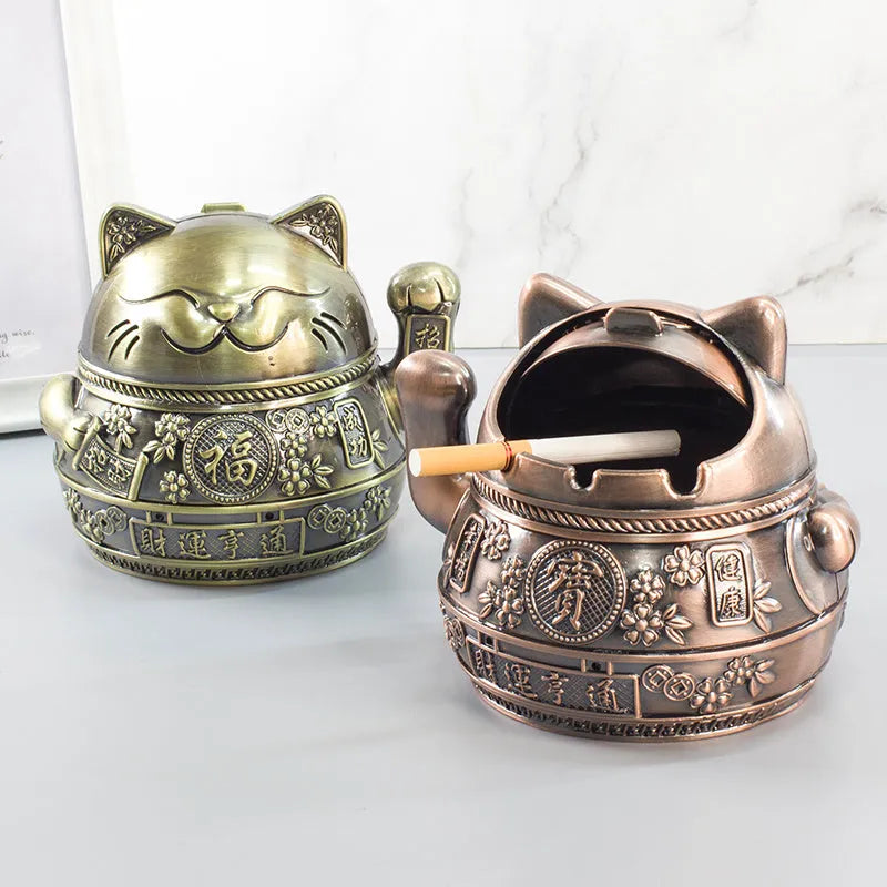 Zinc alloy Lucky Cat ashtray with cover in a gold-black finish on a table