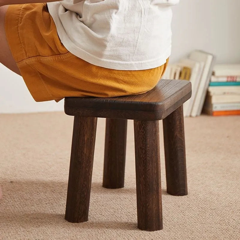 A rustic distressed wooden stool with bracket legs, used as a shoe changing bench in a hallway.