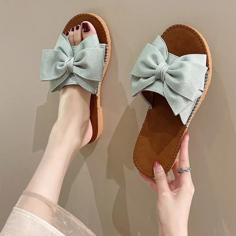 Women's beige suede slip-on sandals with a bow and flat soft rubber sole.