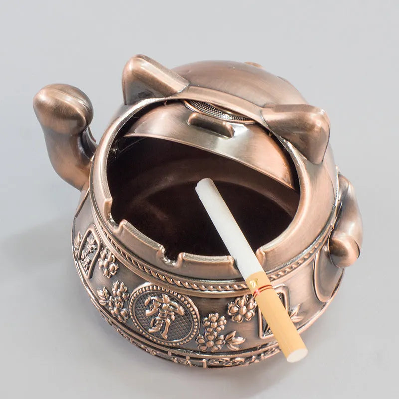 Zinc alloy Lucky Cat ashtray with cover in a gold-black finish on a table