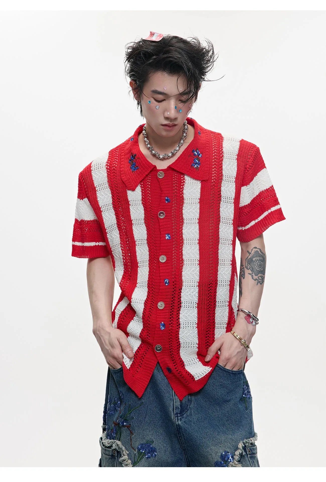 Man wearing a red and black patchwork striped knitted short sleeve shirt with a loose fit.