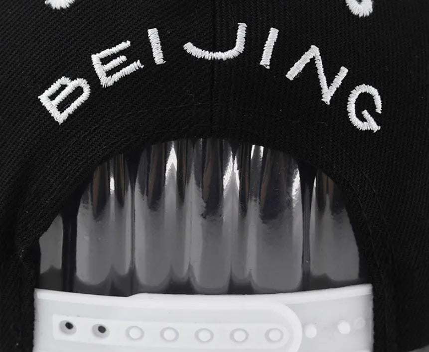 Cotton baseball cap with adjustable strap in black or white, showing embroidered letter detail on the front.