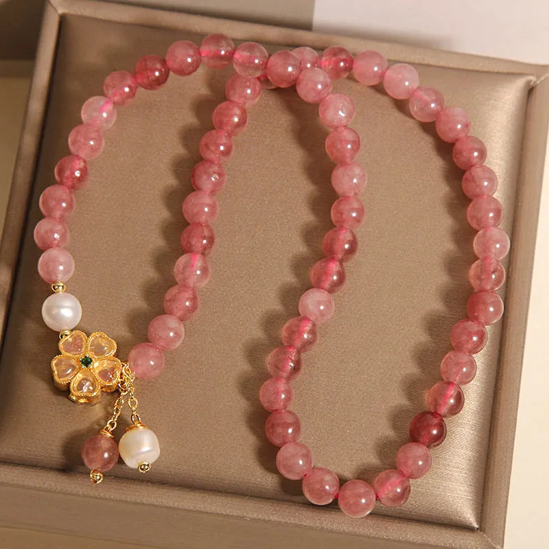 Close-up of a women's bracelet with a strawberry quartz four-leaf clover charm on an alloy chain.