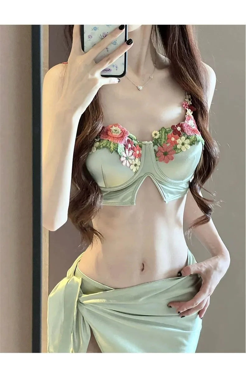 Green women's three-piece bikini swimsuit set with triangle top, briefs, and a short skirt on a mannequin.
